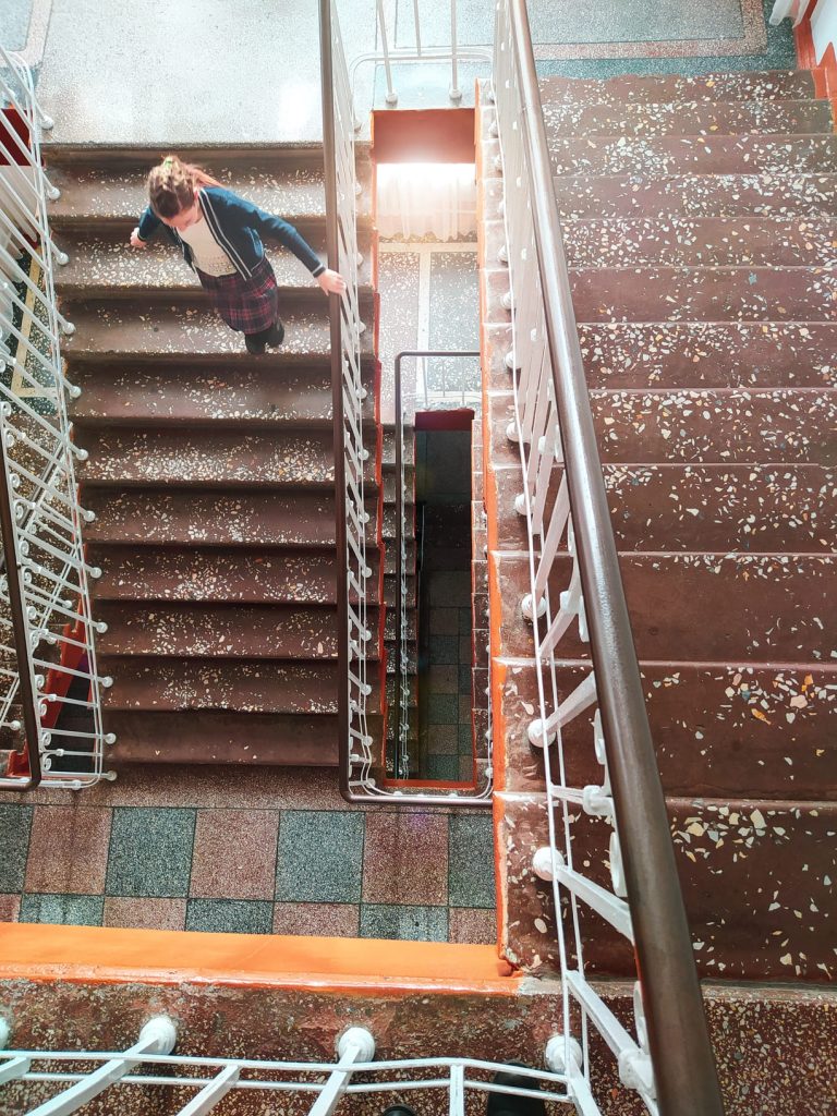 Vista superior de una persona bajando por una escalera de varios tramos en un edificio antiguo.