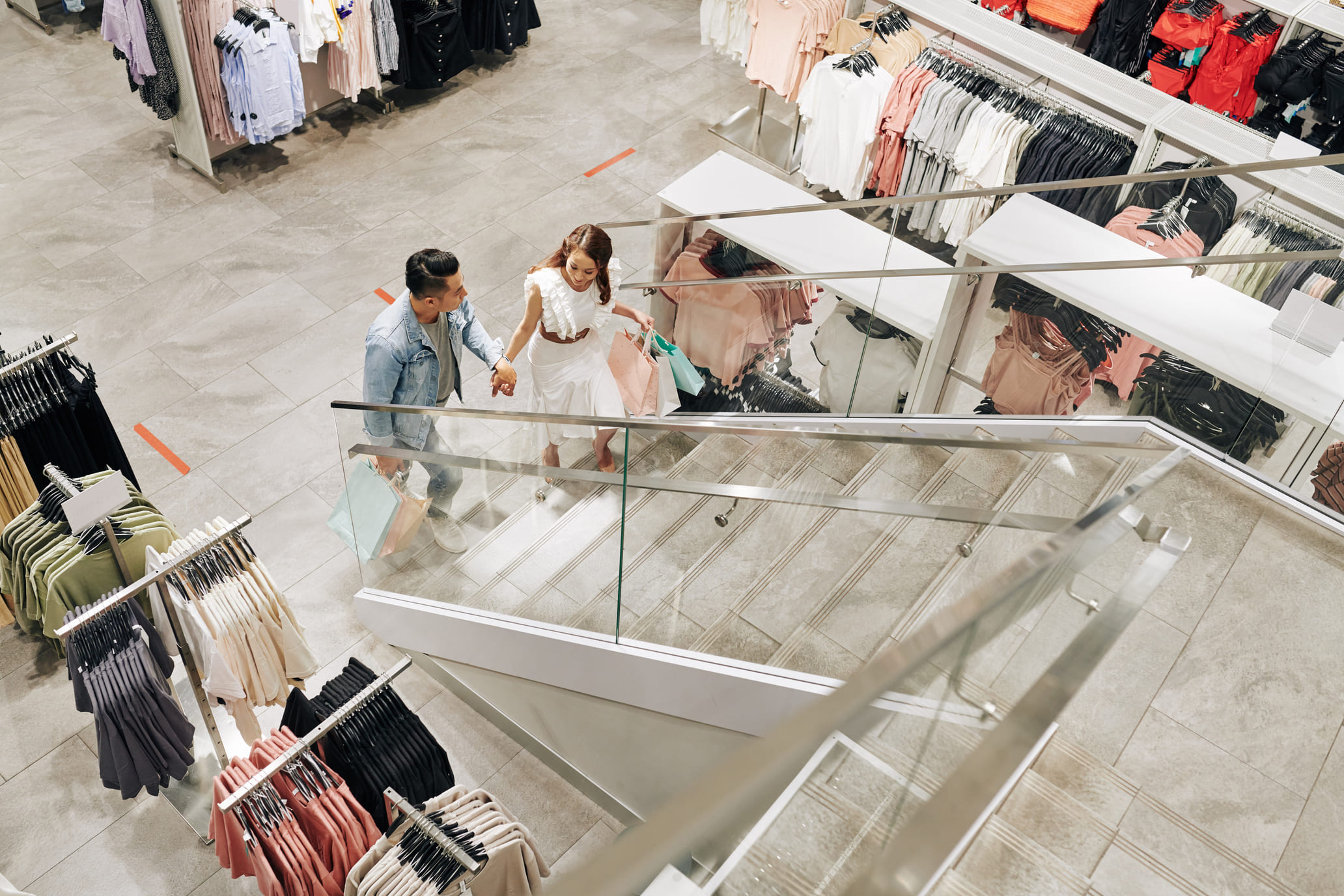 Pareja de compras tomados de la mano en una tienda de ropa moderna desde una vista aérea.