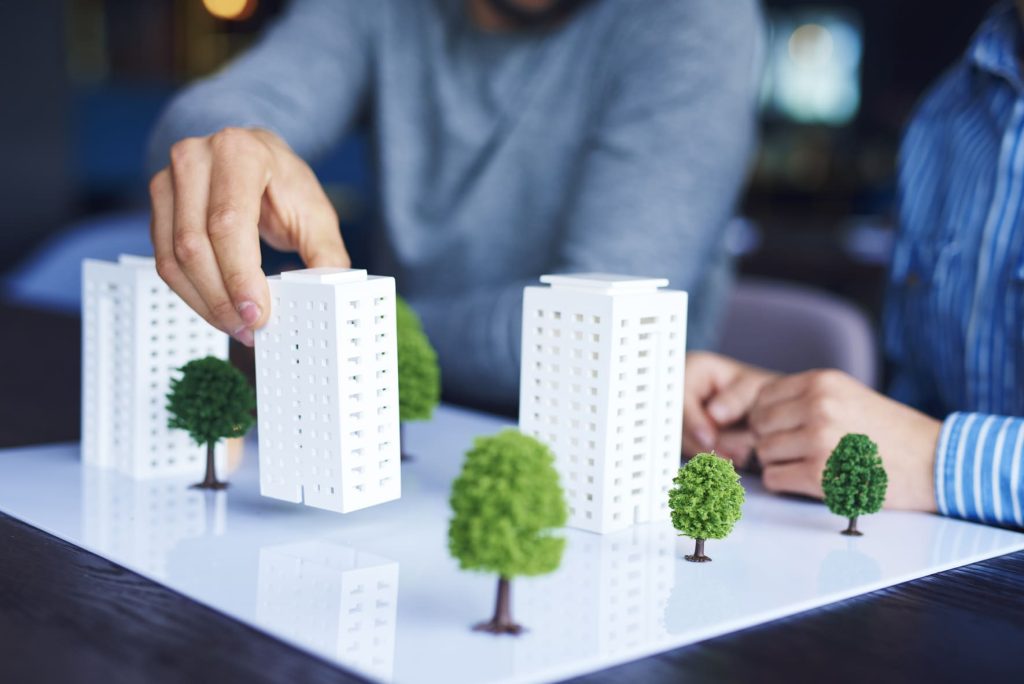 Personas trabajando con un modelo arquitectónico de rascacielos y árboles en miniatura.
